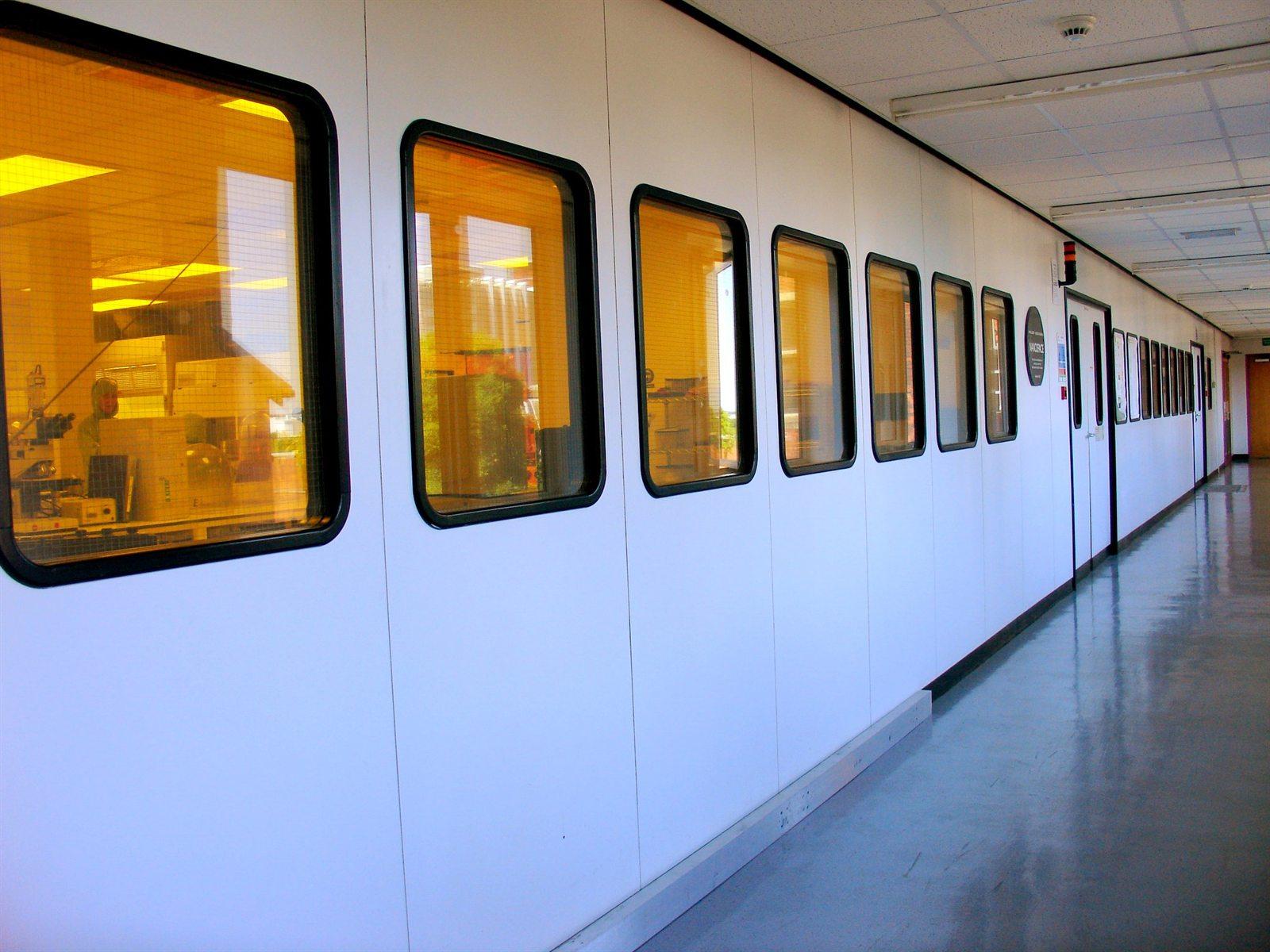 Corridor running alongside a cleanroom, seen through its windows